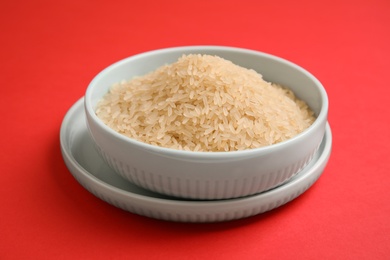 Bowl with uncooked rice on color background