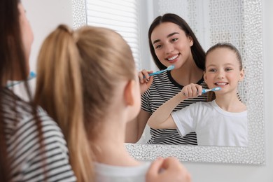 Photo of Mother and her daughter brushing teeth together near mirror in bathroom