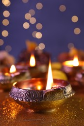 Diwali celebration. Diya lamp on shiny golden table against blurred lights, closeup