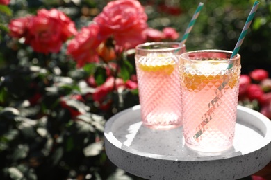 Photo of Glasses of pink lemonade on white table in rose garden. Space for text