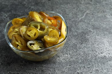 Glass bowl with slices of pickled green jalapeno peppers on grey table, space for text