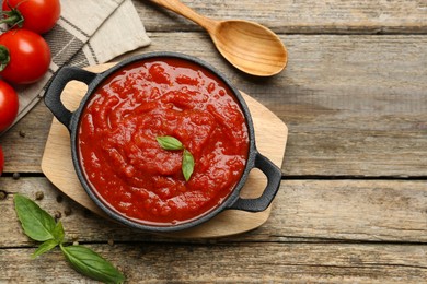 Photo of Homemade tomato sauce in bowl, spoon and fresh ingredients on wooden table, flat lay. Space for text