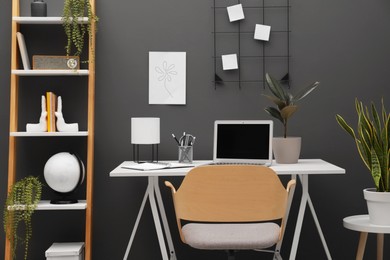 Photo of Cozy workplace with modern laptop on desk and comfortable chair at home