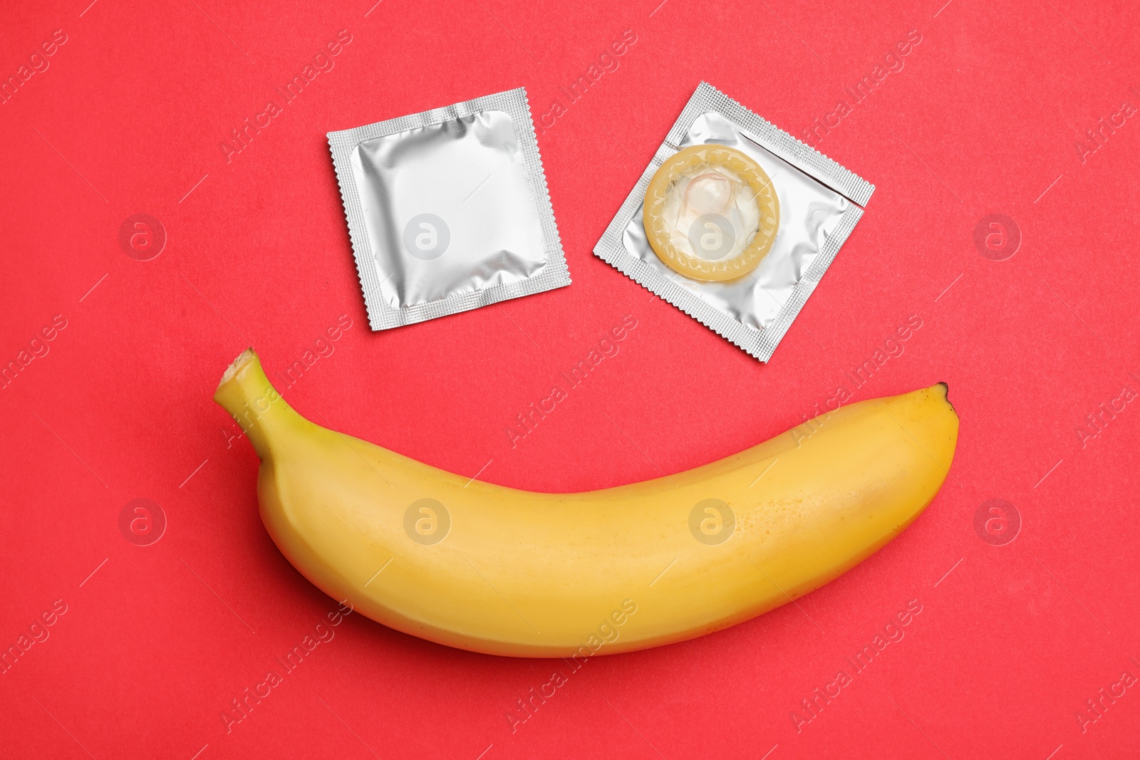 Photo of Condoms with banana on red background, flat lay. Safe sex