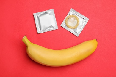 Condoms with banana on red background, flat lay. Safe sex