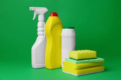 Photo of Different cleaning supplies and sponges on green background