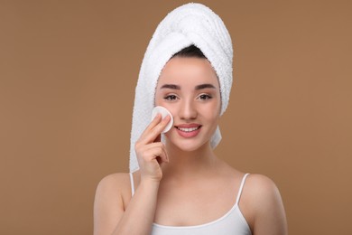 Photo of Beautiful woman in terry towel removing makeup with cotton pad on beige background