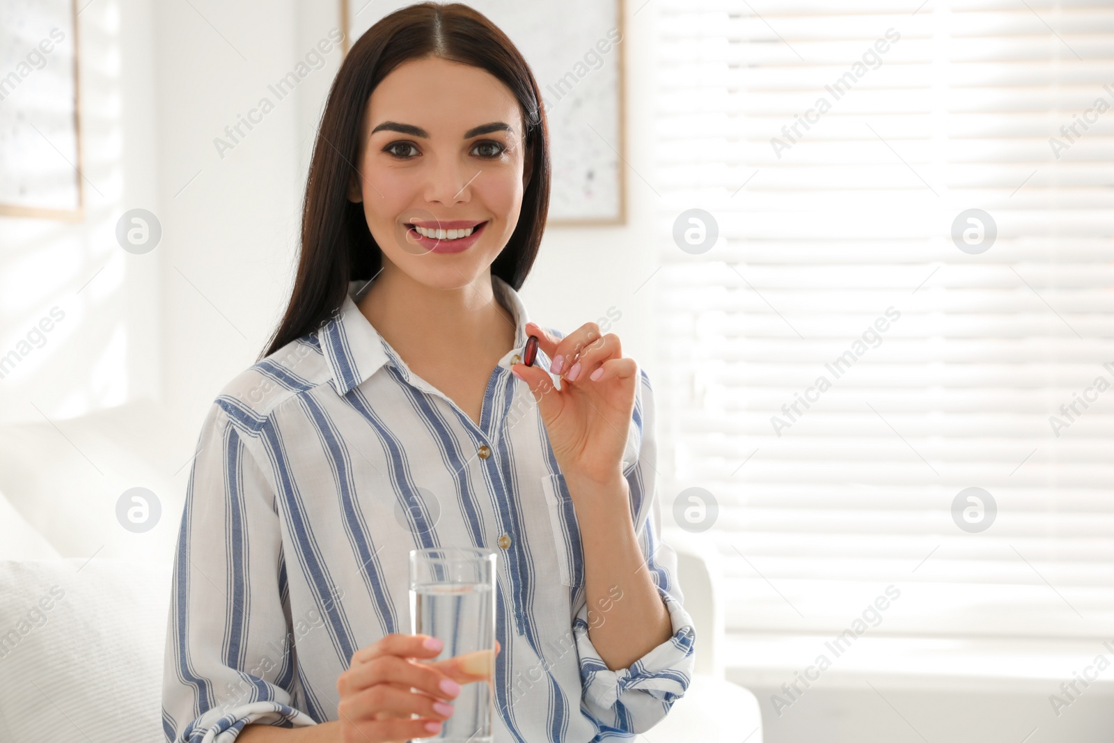 Photo of Young woman with glass of water and vitamin capsule indoors. Space for text