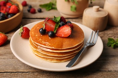 Photo of Stack of tasty pancakes with fresh berries and mint on wooden table, closeup