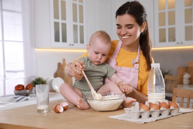 Photo of Happy young woman and her cute little baby making dough together in kitchen, space for text