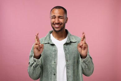 Photo of Happy man crossing his fingers on pink background