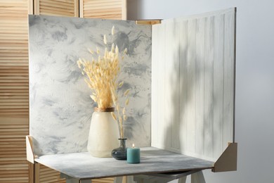 Photo of Vases with beautiful dry flowers, candle and double-sided backdrops on table in photo studio