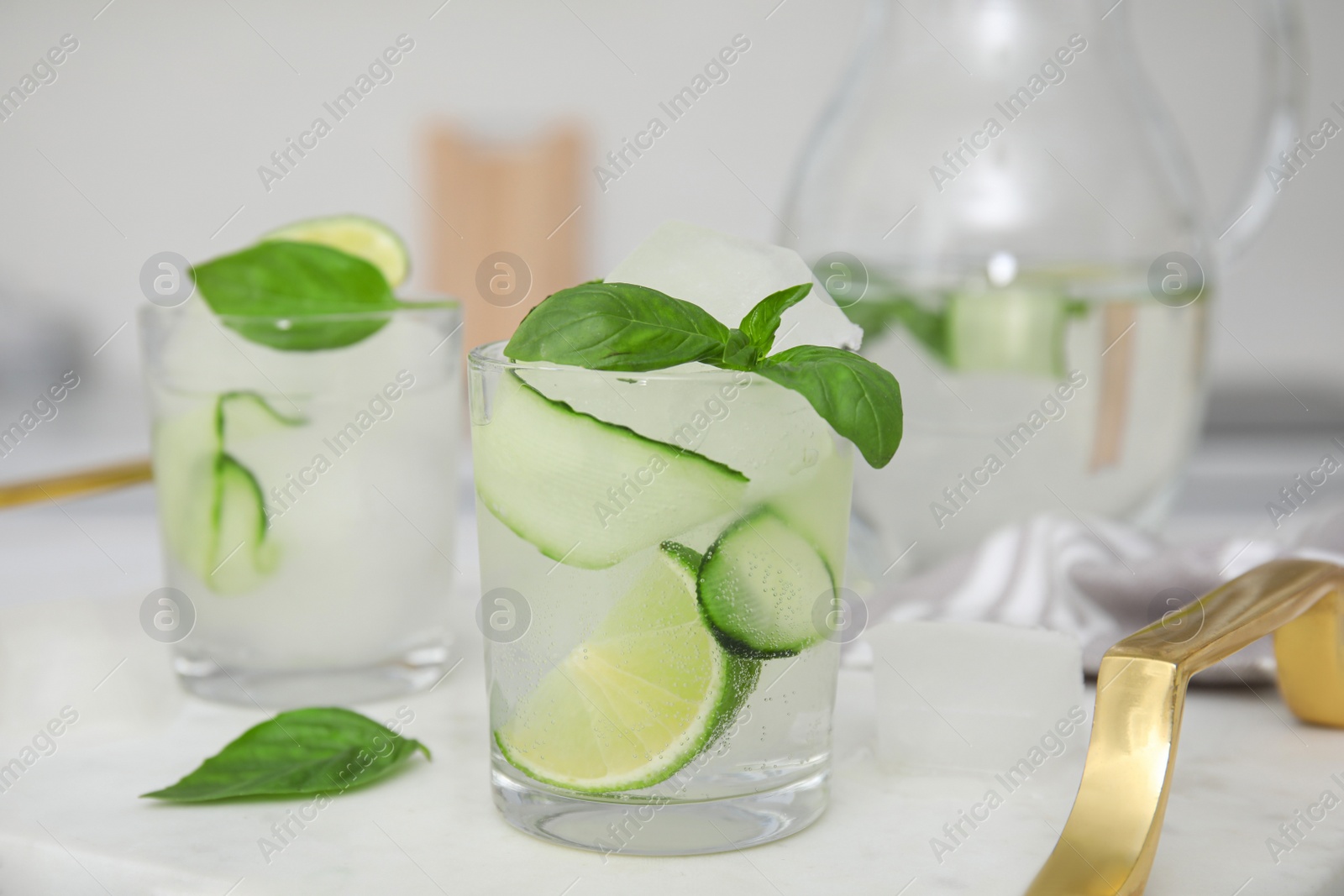 Photo of Tasty fresh cucumber water with sliced lime and basil on white table indoors