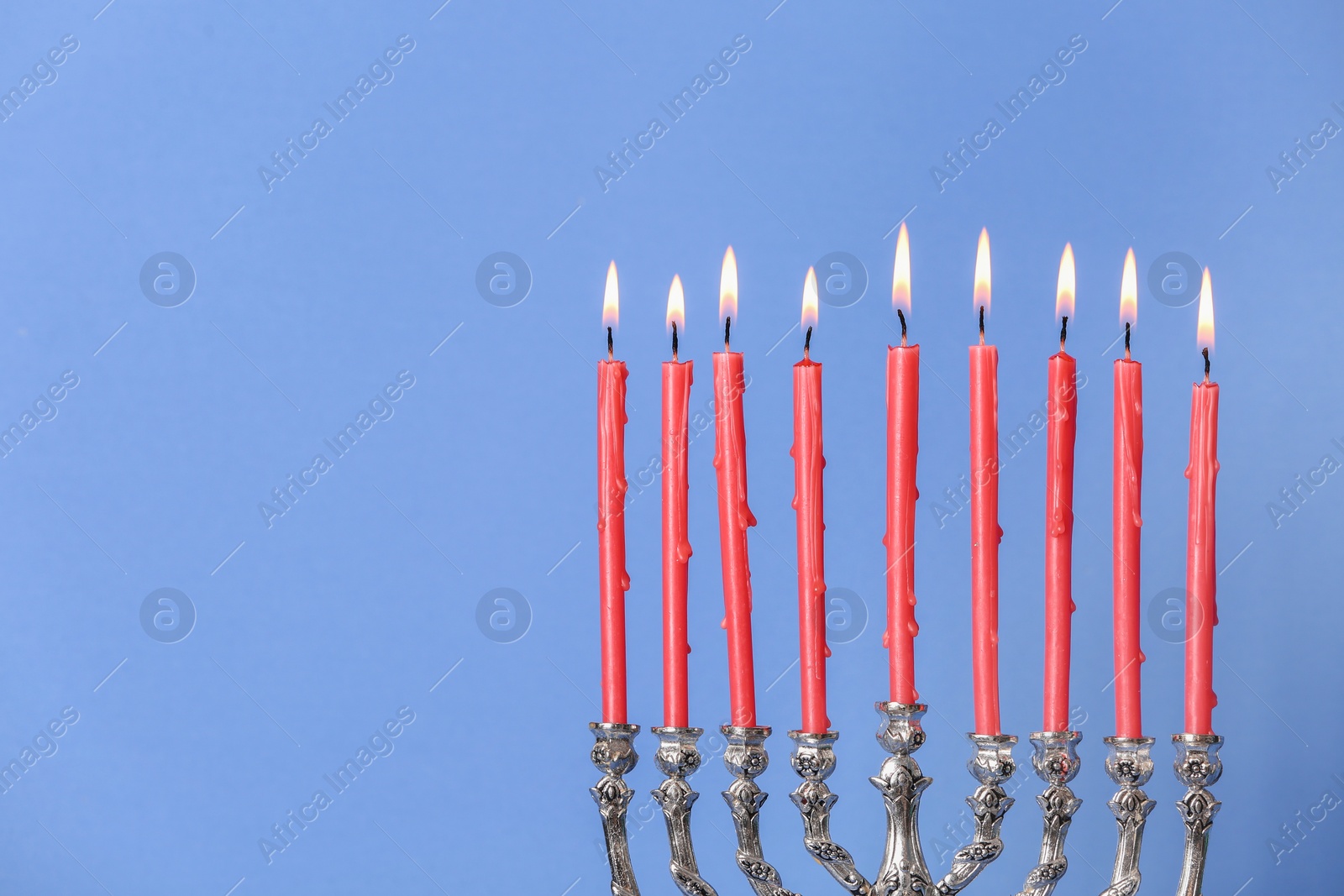 Photo of Silver menorah with burning candles on light blue background, space for text. Hanukkah celebration