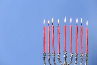 Photo of Silver menorah with burning candles on light blue background, space for text. Hanukkah celebration