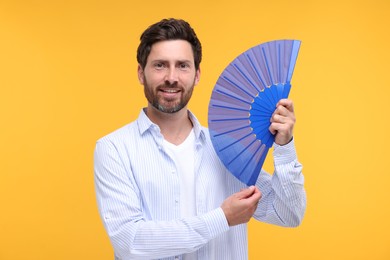 Photo of Happy man holding hand fan on orange background