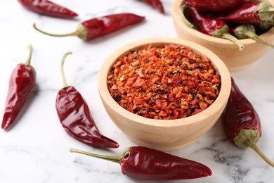 Photo of Chili pepper flakes in bowl and pods on white marble table, closeup