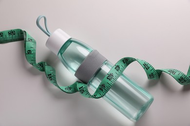 Measuring tape and bottle with water on white background, flat lay. Weight control concept