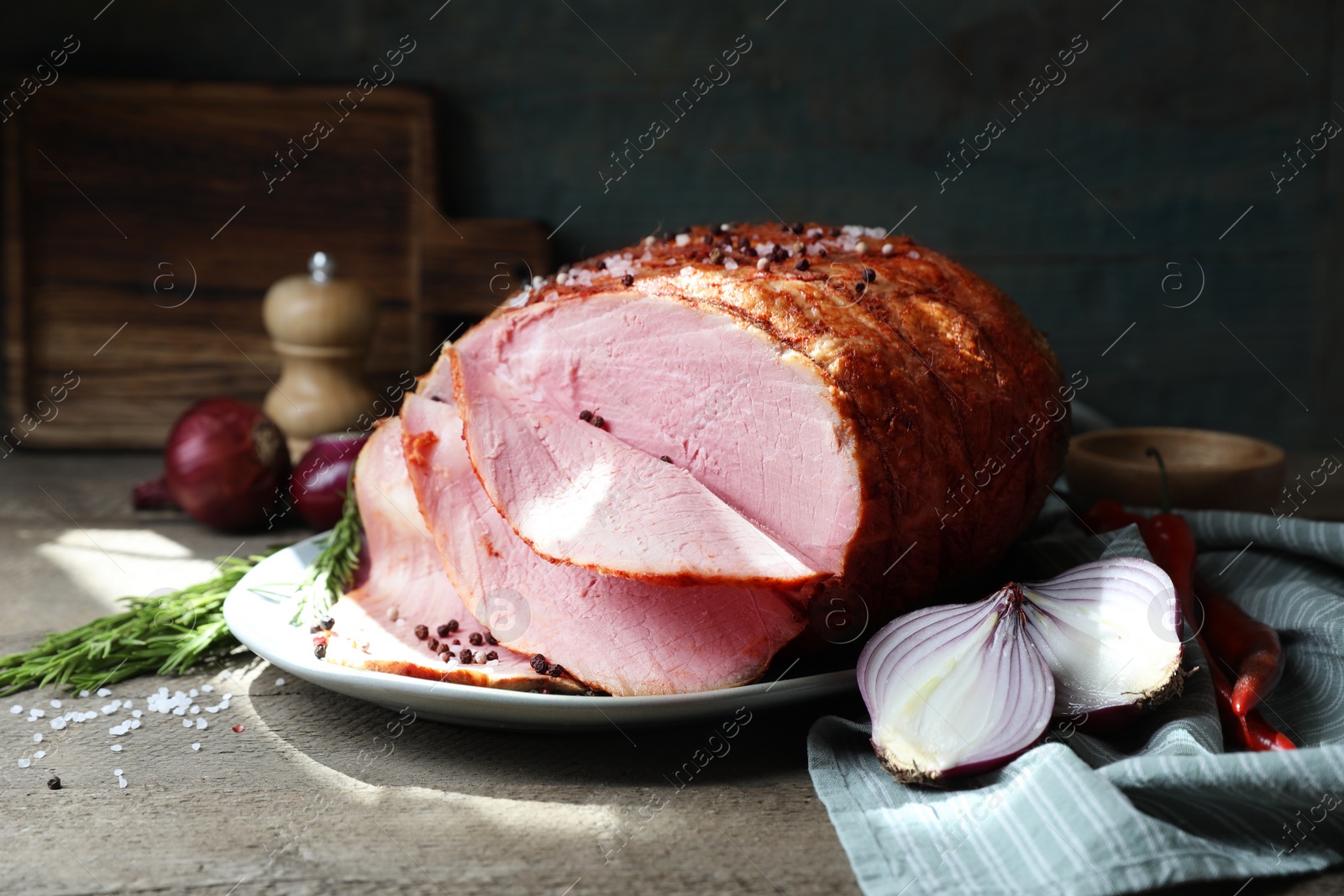 Photo of Delicious baked ham, onion, chili peppers and rosemary on grey wooden table, closeup