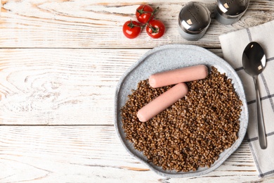 Flat lay composition with tasty buckwheat porridge and sausages on white wooden table, space for text