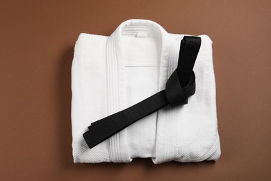 Black karate belt and kimono on brown background, top view