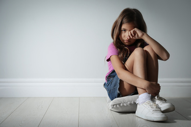 Photo of Sad little girl near white wall, space for text. Domestic violence concept