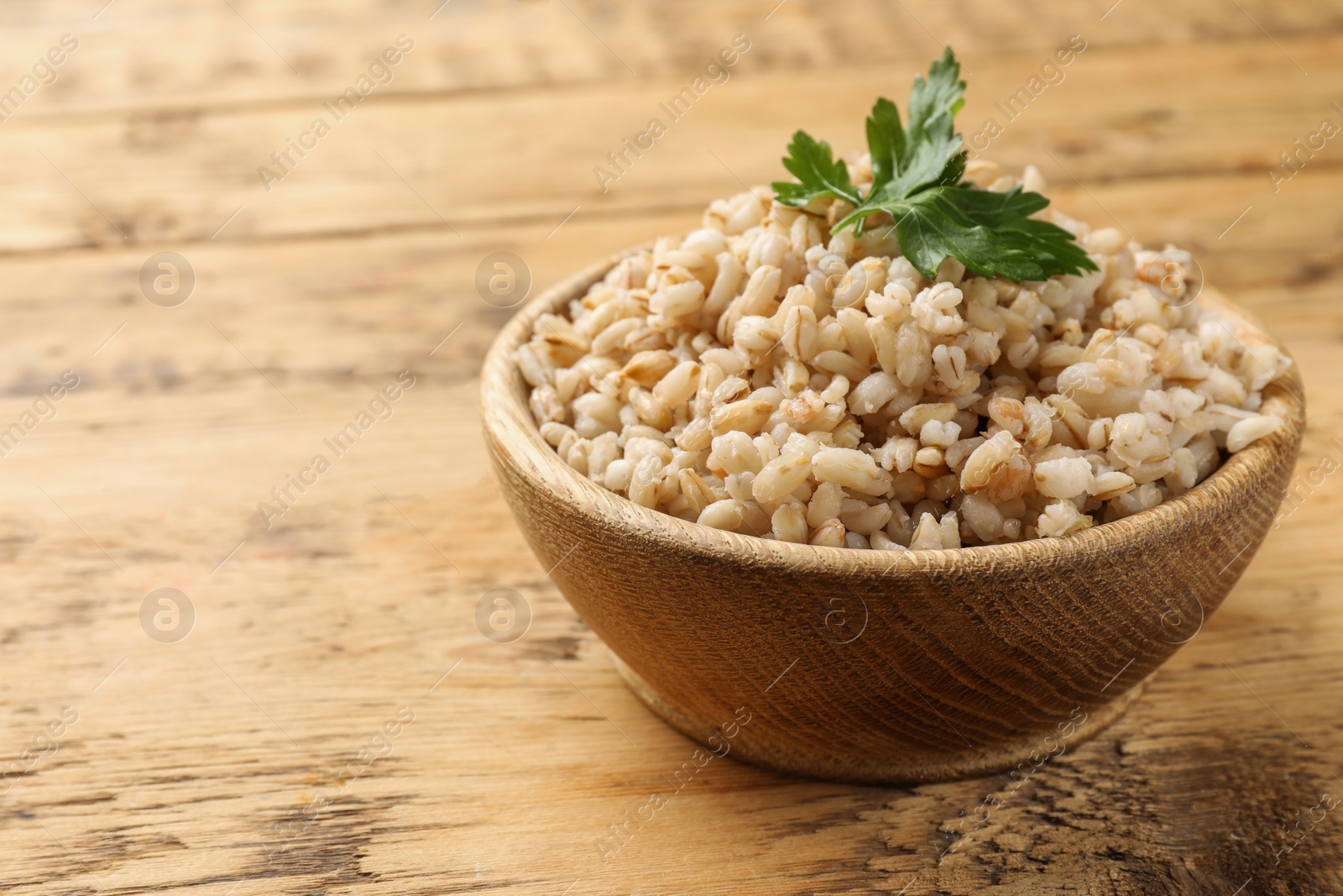 Photo of Delicious pearl barley with parsley in bowl on wooden table, closeup. Space for text