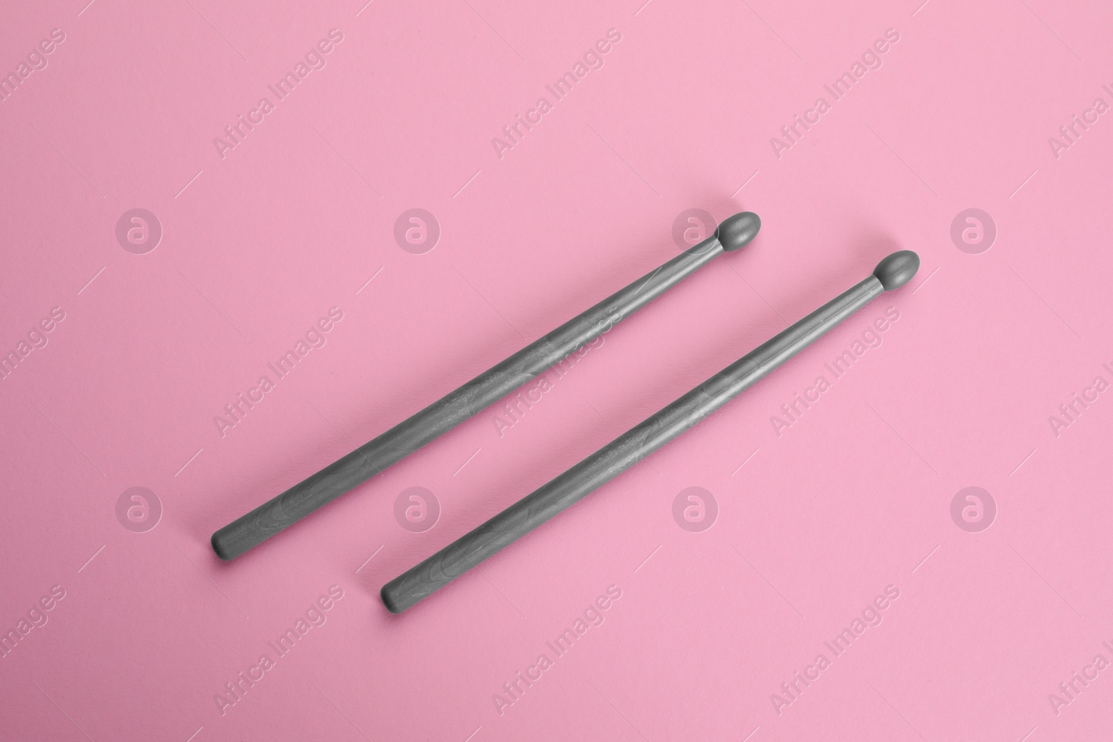 Photo of Two grey drumsticks on pink background, top view