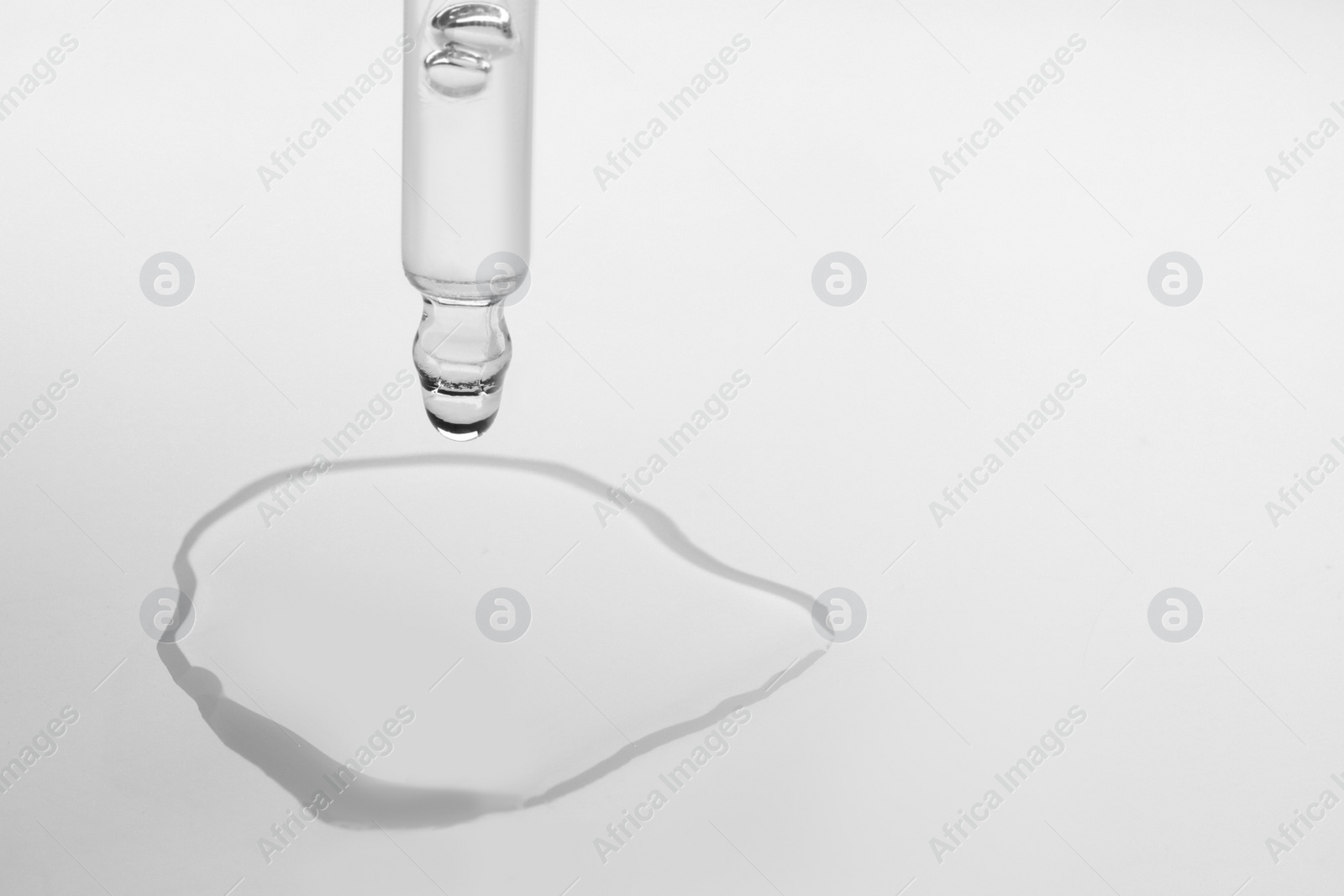 Photo of Dripping face serum from pipette on white background, closeup. Space for text