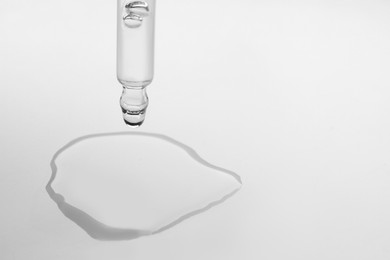 Photo of Dripping face serum from pipette on white background, closeup. Space for text