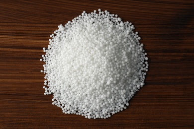 Photo of Pellets of ammonium nitrate on wooden table, flat lay. Mineral fertilizer