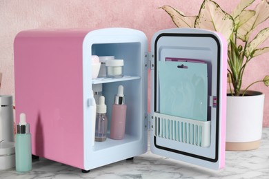 Photo of Open cosmetic refrigerator and skin care products on white marble table