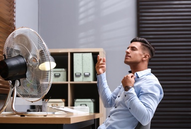 Photo of Man enjoying air flow from fan at workplace