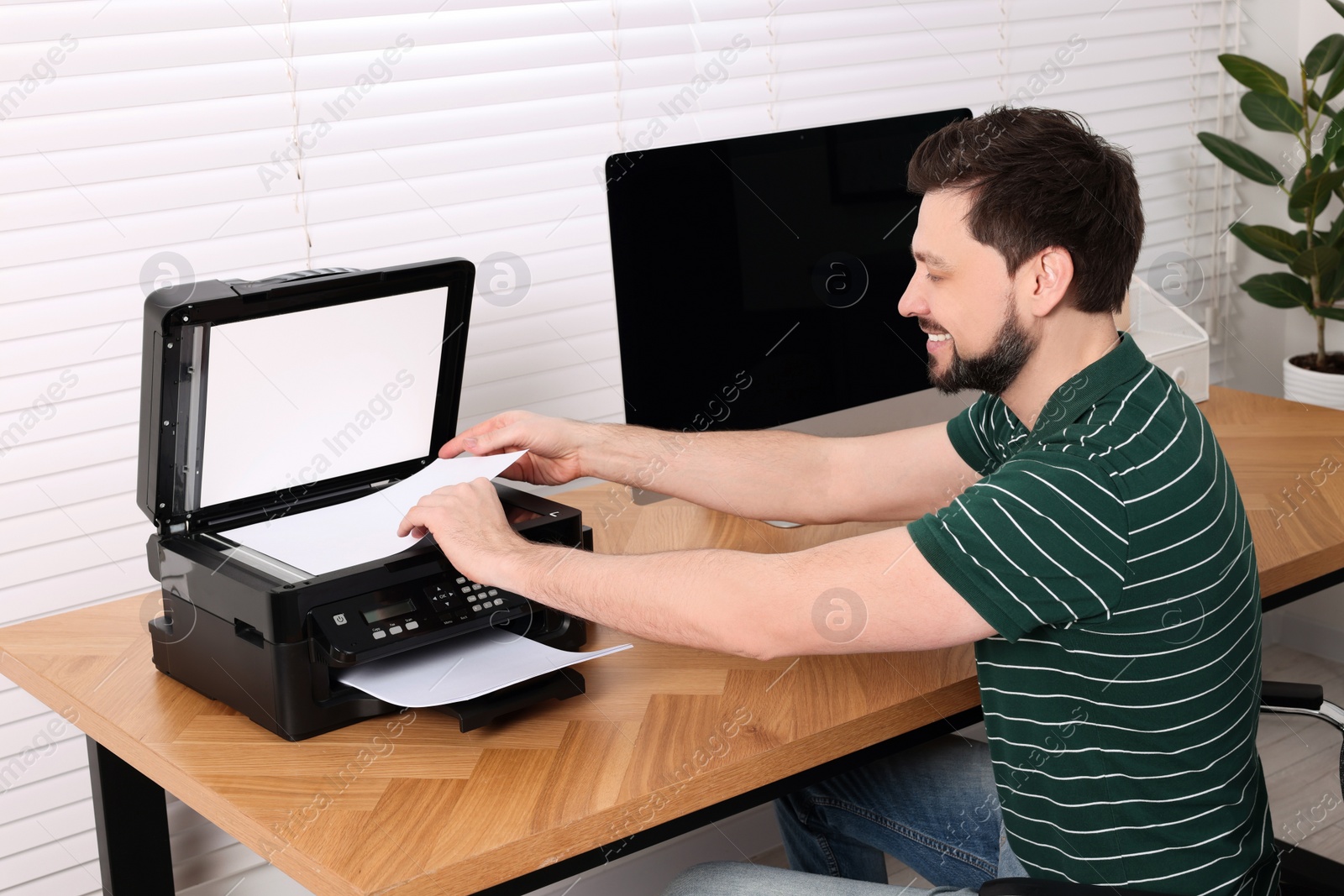 Photo of Man using modern printer at wooden table indoors