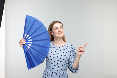 Happy woman with blue hand fan pointing on light grey background