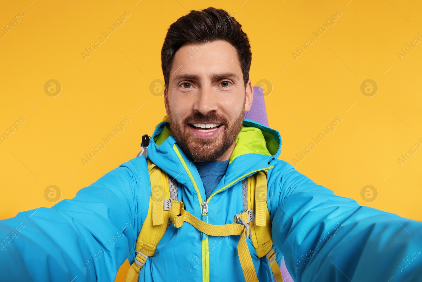 Photo of Happy man with backpack taking selfie on orange background. Active tourism