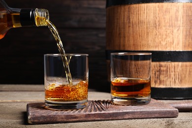 Photo of Pouring whiskey into glass from bottle near wooden barrel on table