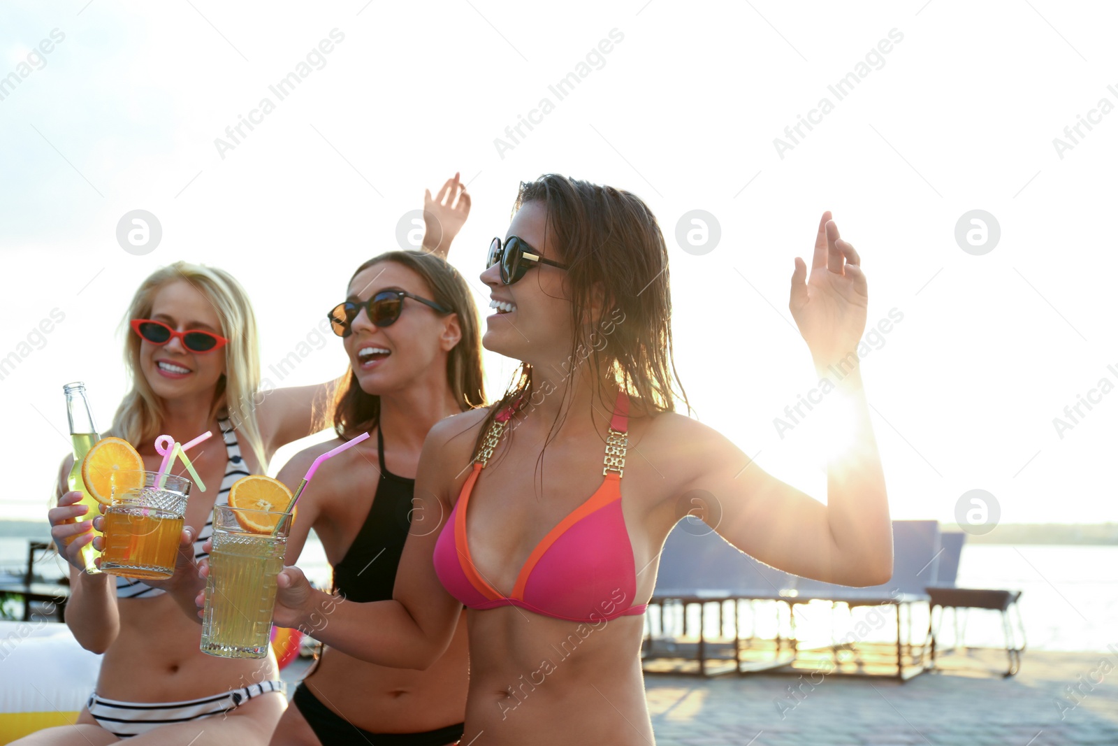 Photo of Happy women in swimwear with refreshing drinks enjoying fun party outdoors