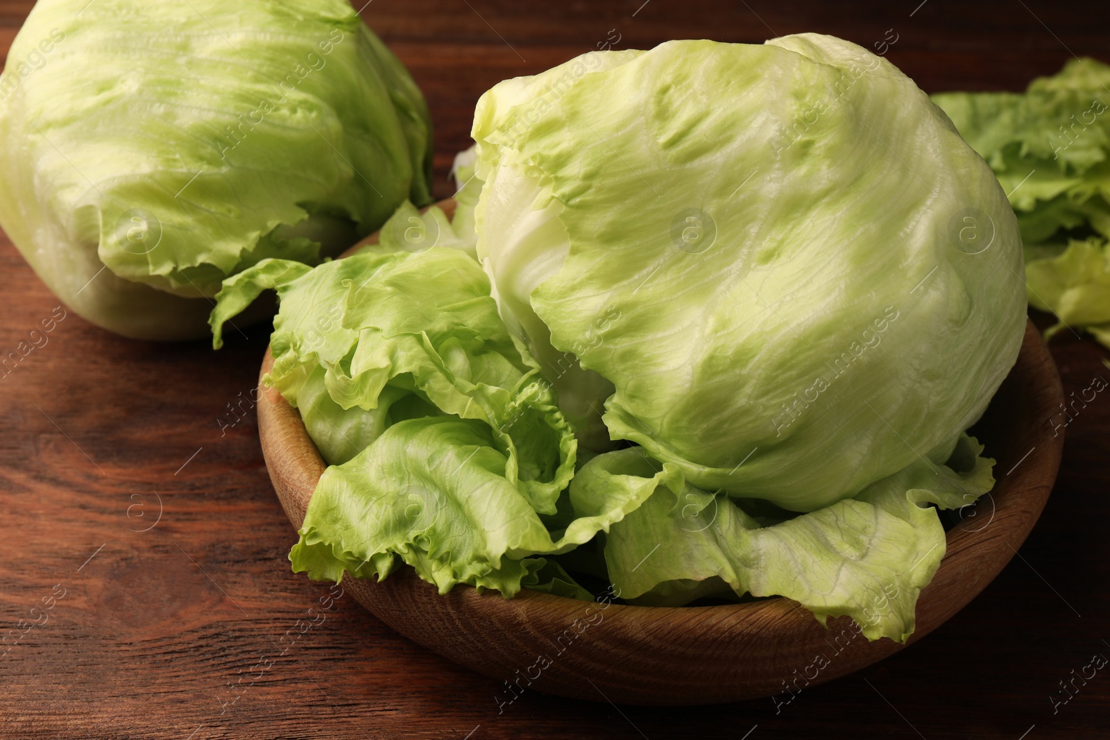 Photo of Fresh green iceberg lettuce heads and leaves on wooden table, closeup