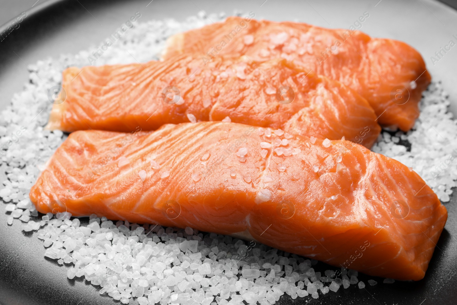 Photo of Fresh raw salmon with salt on black plate, closeup