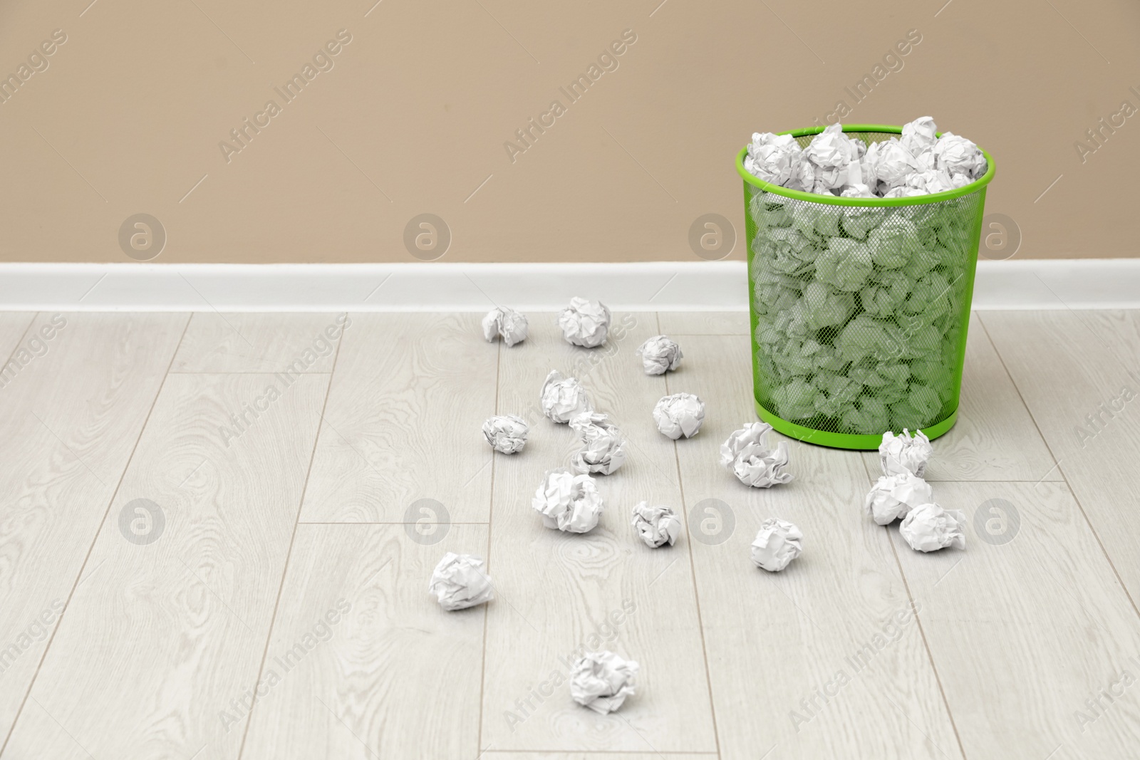 Photo of Metal bin and crumpled paper on floor near color wall, space for text