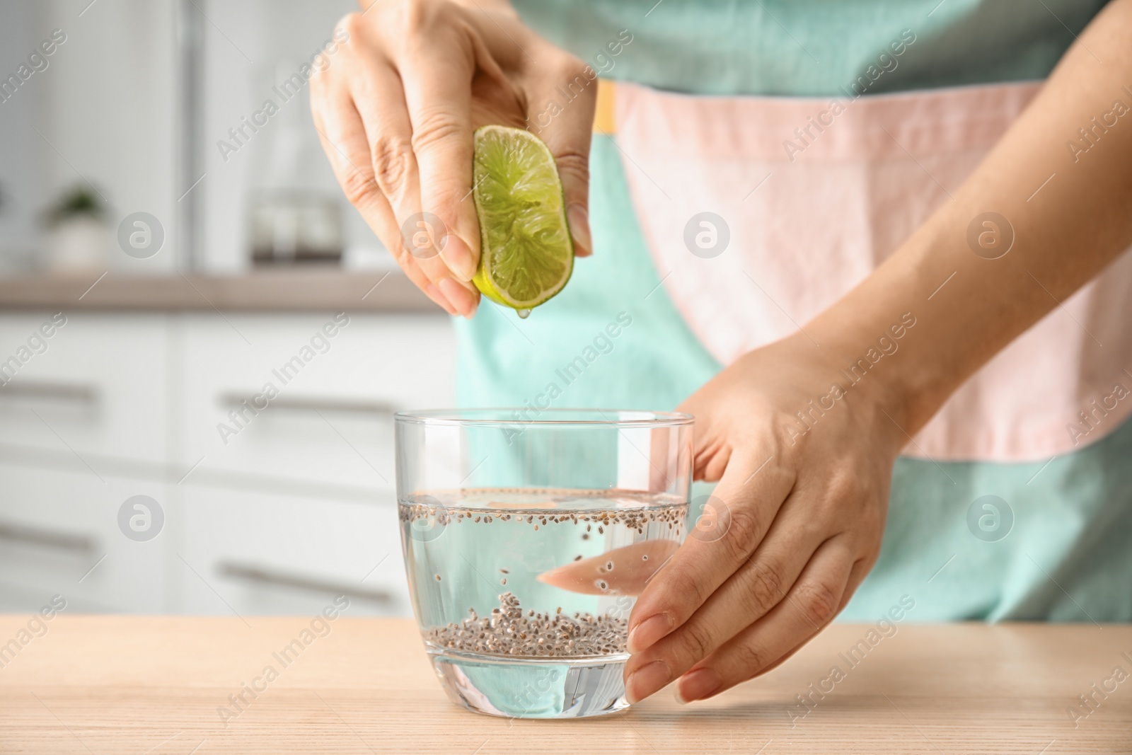 Photo of Young woman squeezing lime into glass of water with chia seeds on table, closeup