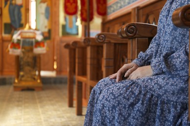 Mature woman sitting on wooden bench in church, closeup. Space for text
