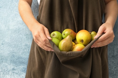 Woman in apron with ripe pears on color background, closeup