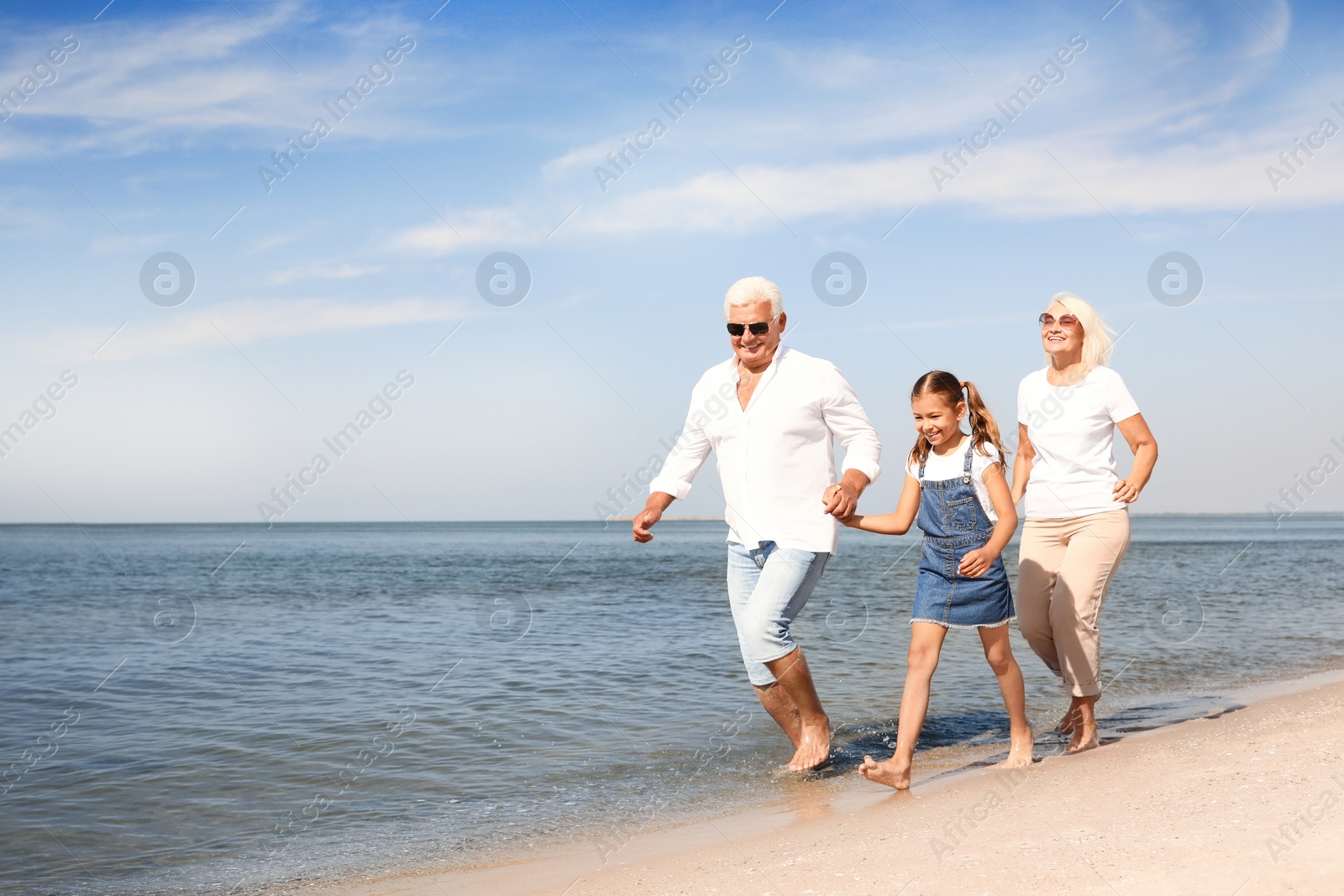 Photo of Cute little girl with grandparents spending time together on sea beach