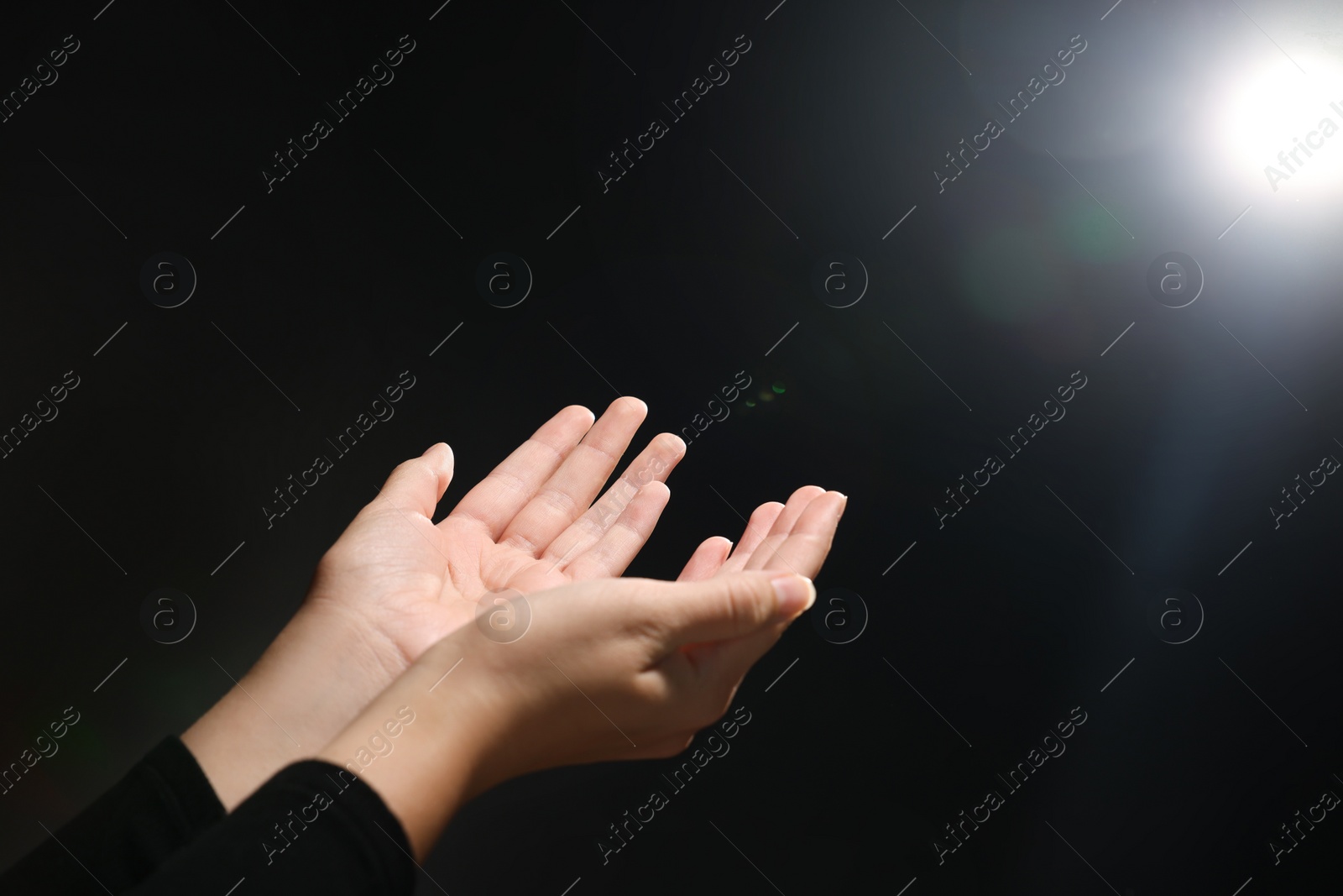 Photo of Woman stretching hands towards light in darkness, closeup