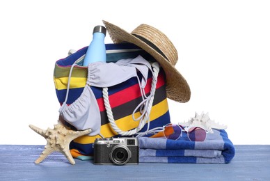 Photo of Stylish bag, camera and other beach accessories on grey wooden table against white background