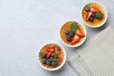 Photo of Delicious creme brulee with berries and mint in bowl on grey textured table, top view. Space for text