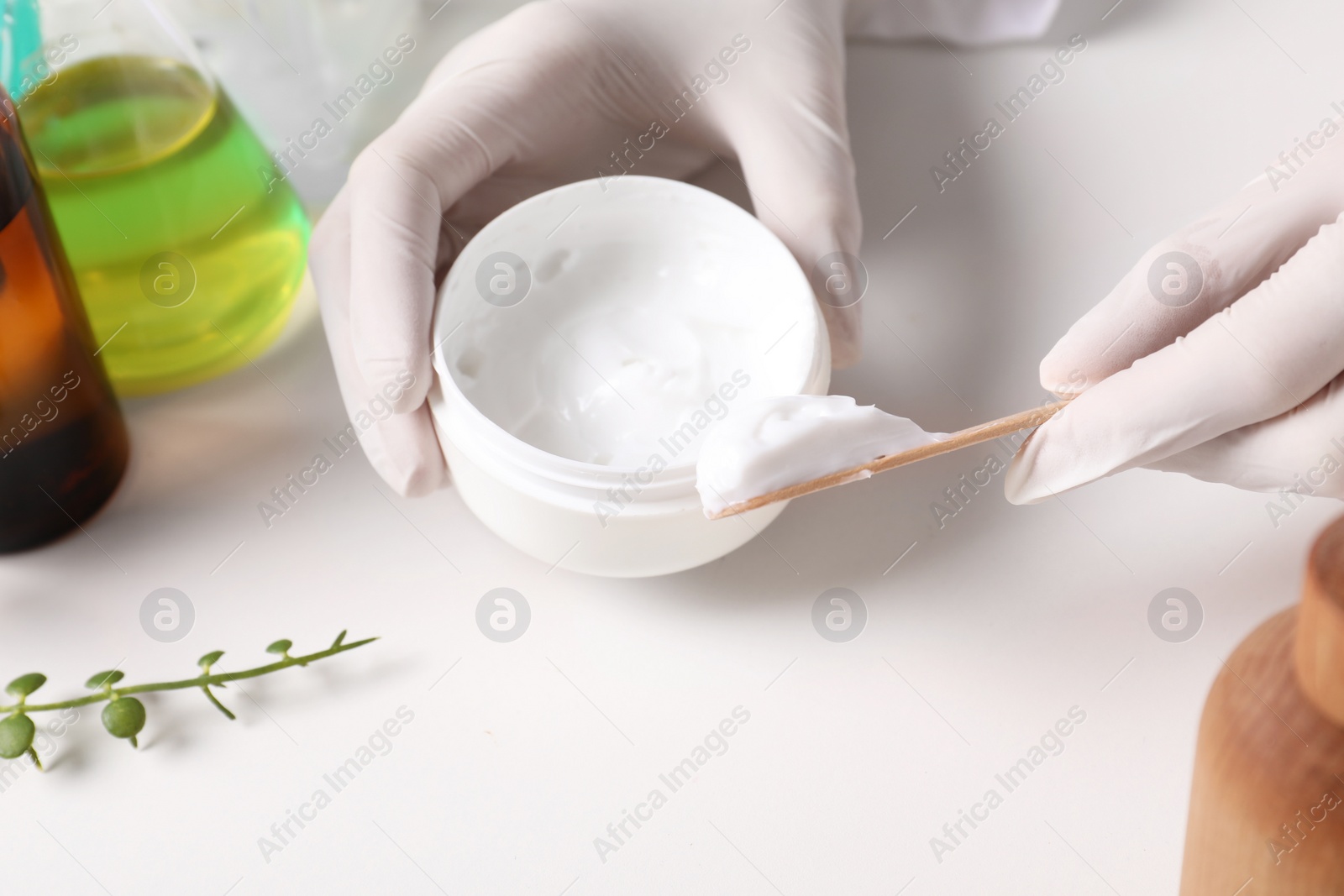 Photo of Dermatologist with jar testing cosmetic product at white table, closeup