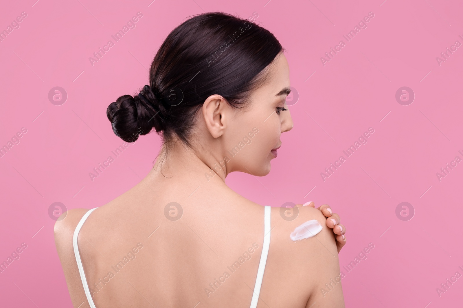 Photo of Beautiful woman with smear of body cream on her shoulder against pink background, back view